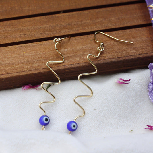 Mystical Eye SwirlsMaterial info: Evil eye wavy dangle earrings Beads: 6mm evil eye bead Wire: Tarnish resistant, 20-gauge gold copper Protective talismans, often called "evil eye charms," are believed to ward off the negative effects of the evil eye and